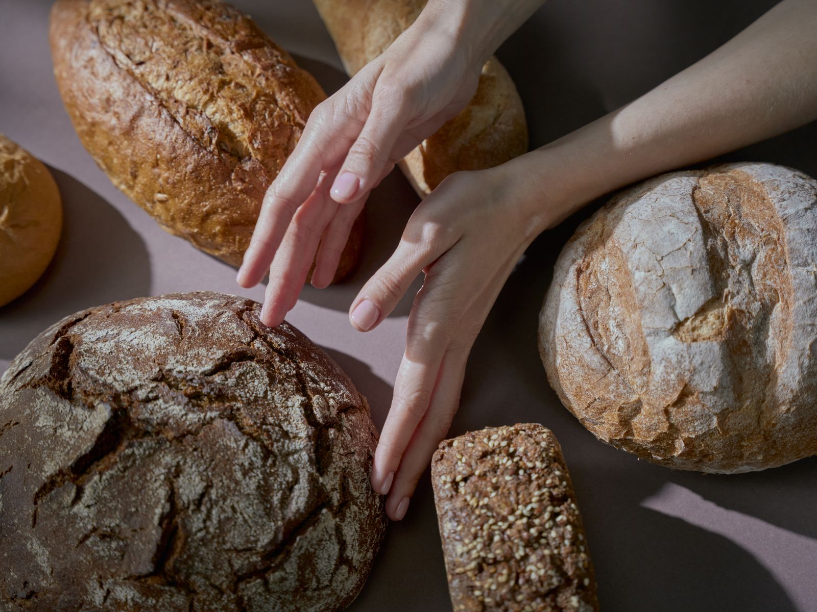 Des mains effleurent une variété de pains faits maison dans une ambiance chaleureuse.
