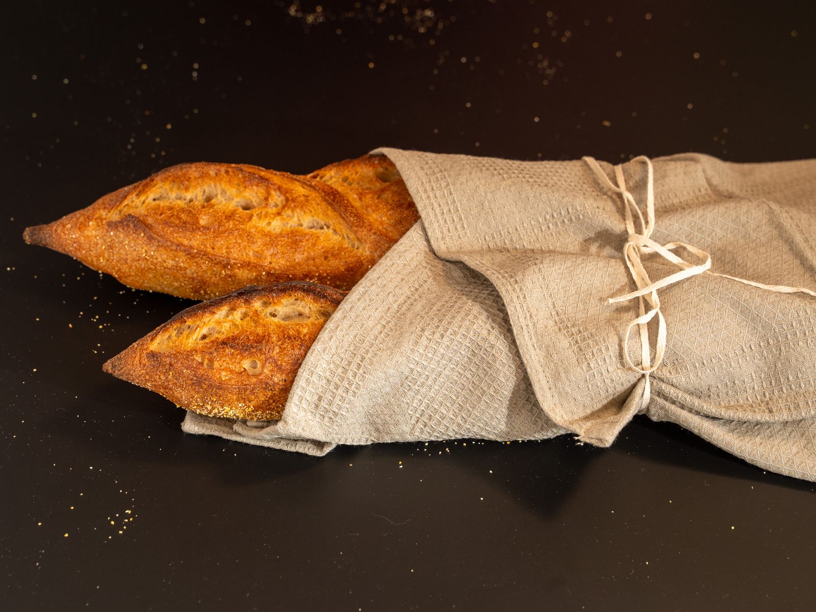 Deux baguettes artisanales fraîchement cuites, enveloppées dans un torchon en lin sur un fond sombre.