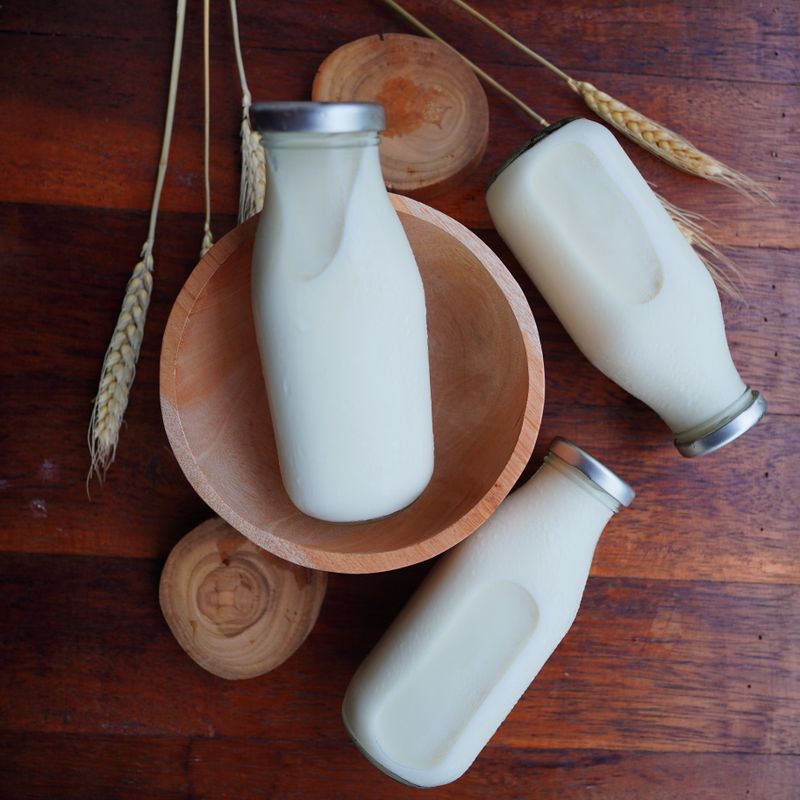 Trois bouteilles de lait en verre disposées sur une table en bois avec décor rustique.