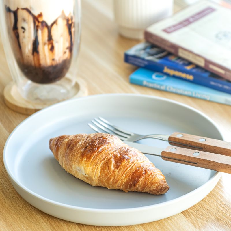 Croissant frais accompagné d'un café glacé et de livres sur une table en bois.