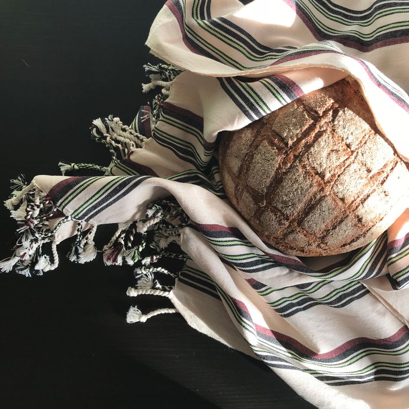 Pain rond artisanal sur une table sombre, enveloppé d’un tissu rayé, éclairage naturel.