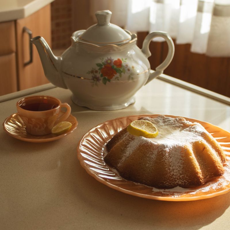 Scène chaleureuse d'une théière, d'un thé au citron et d'un cake sur un plan de travail de cuisine.