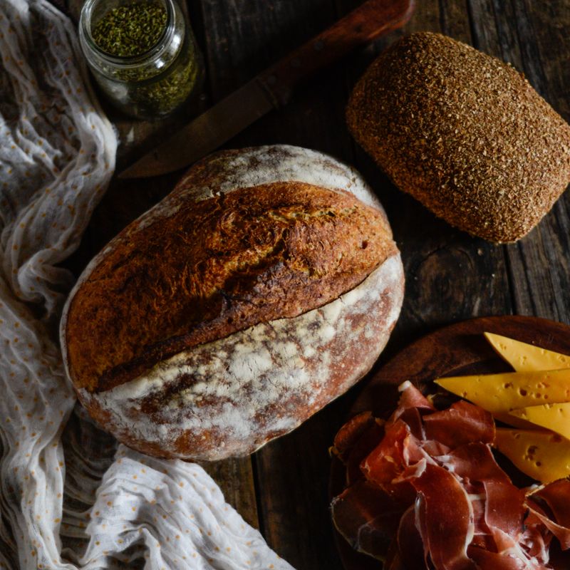 Vue de dessus d’un pain rustique, fromage et jambon sur une table en bois avec des herbes.